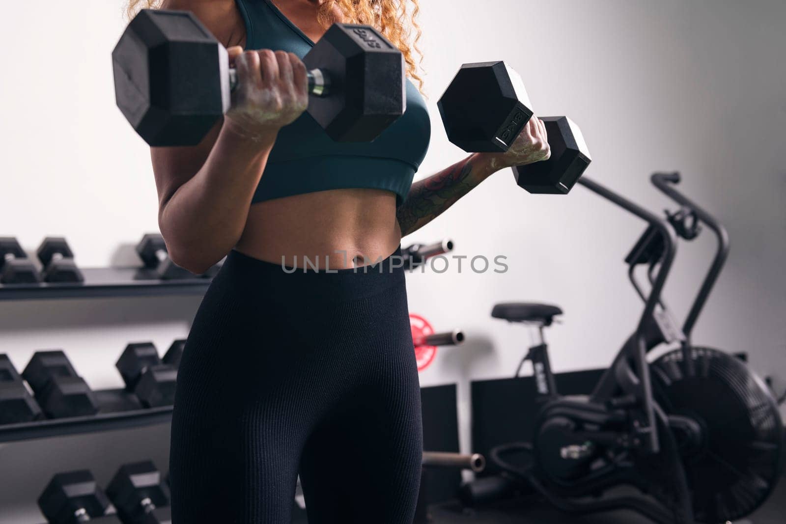 crop of unrecognizable strong sportswoman doing exercise on biceps with dumbbells during workout at gym, concept of fitness and active lifestyle
