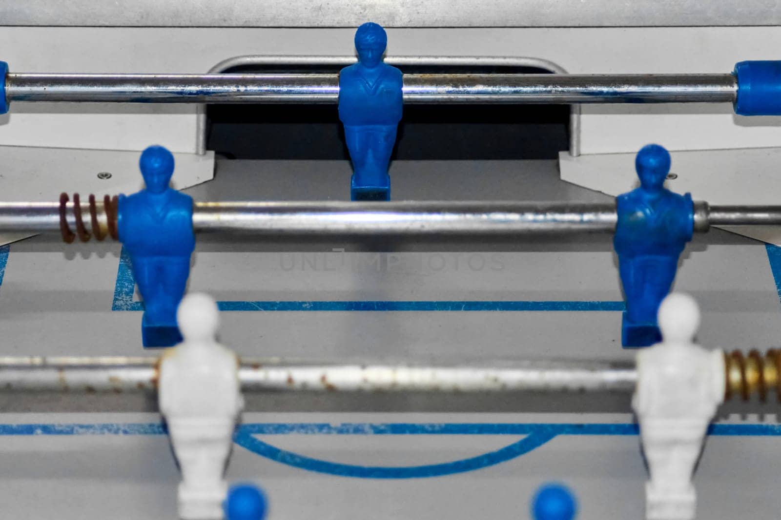 The image highlights foosball players on a grey playing field with blue lines. The vibrant colors and action pose of the figures emphasize the excitement of table soccer.