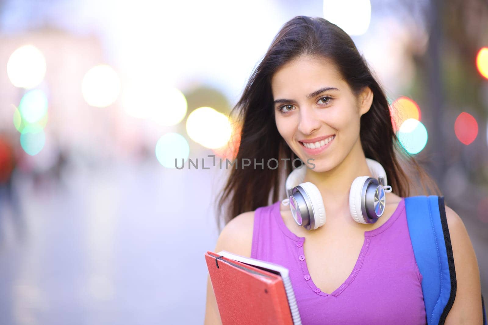 Front view portrait of a happy student posing in the street looking at camera