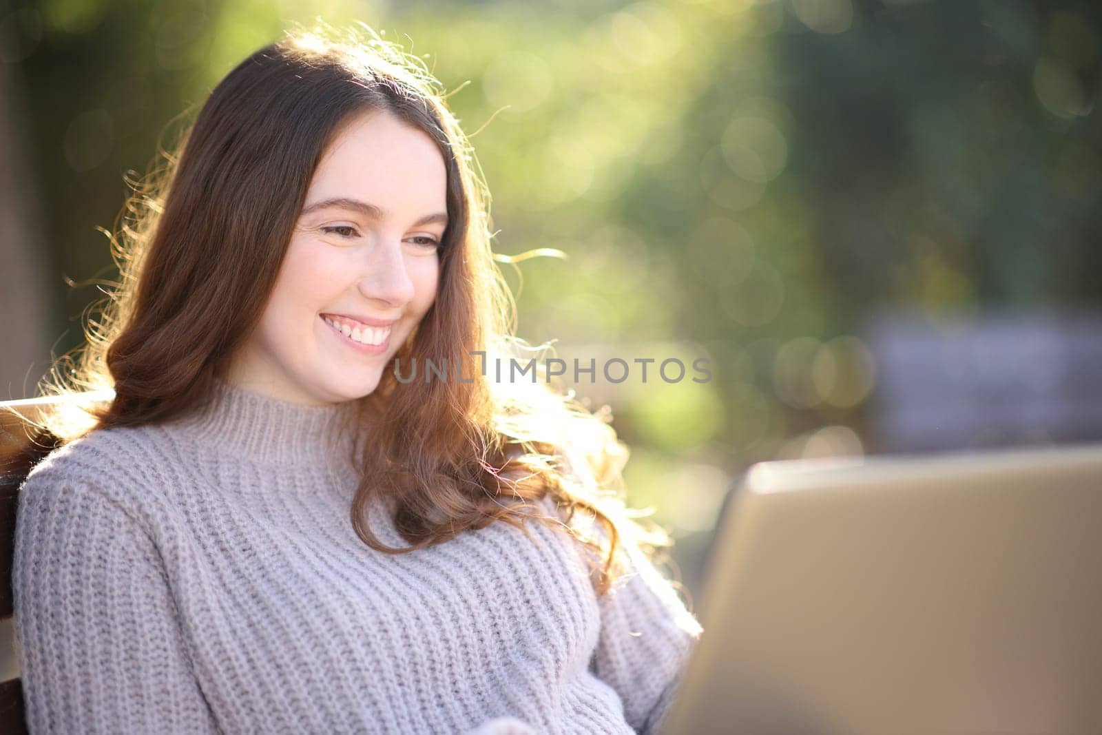Happy woman is using laptop sitting on a bench in a park