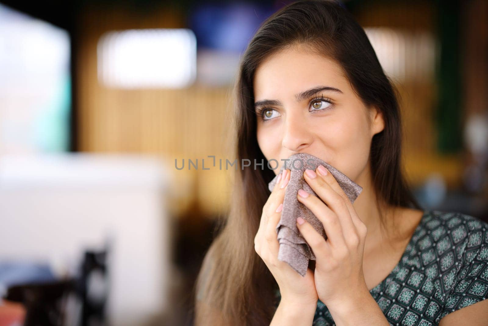 Woman cleaning mouth with napkin sitting in a restaurant looking away