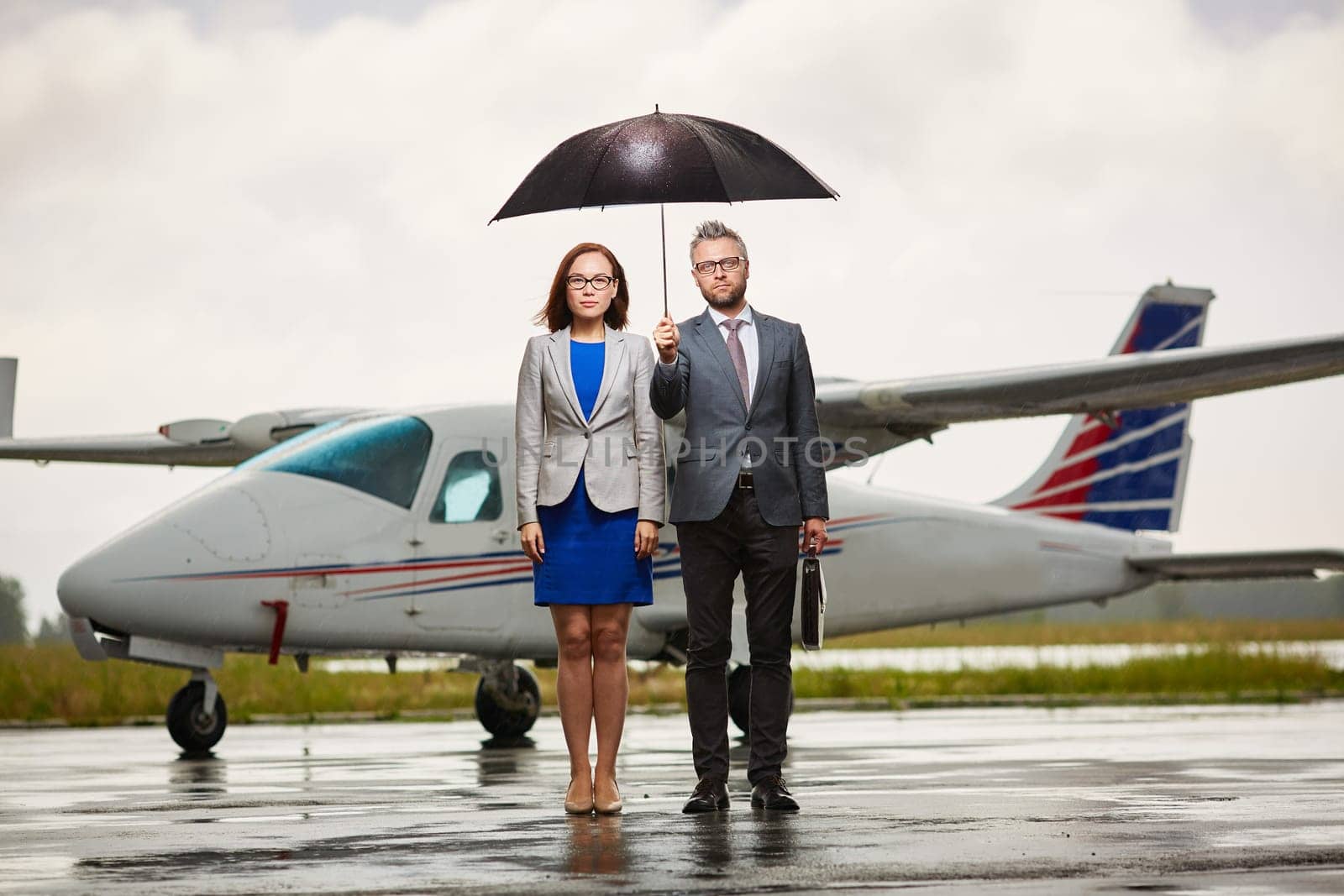 Two business leaders under umbrella looking at camera on rainy day