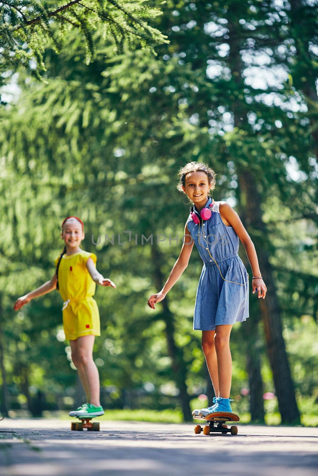 Cute girl and her friend skateboarding on summer weekend