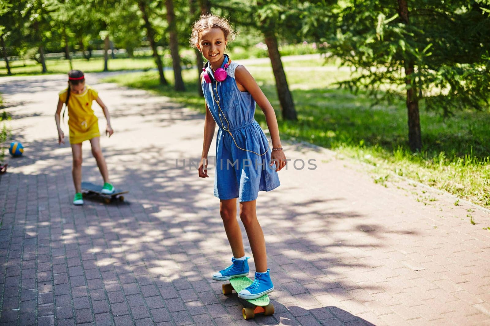 Little girl skateboarding in park with her friend on background
