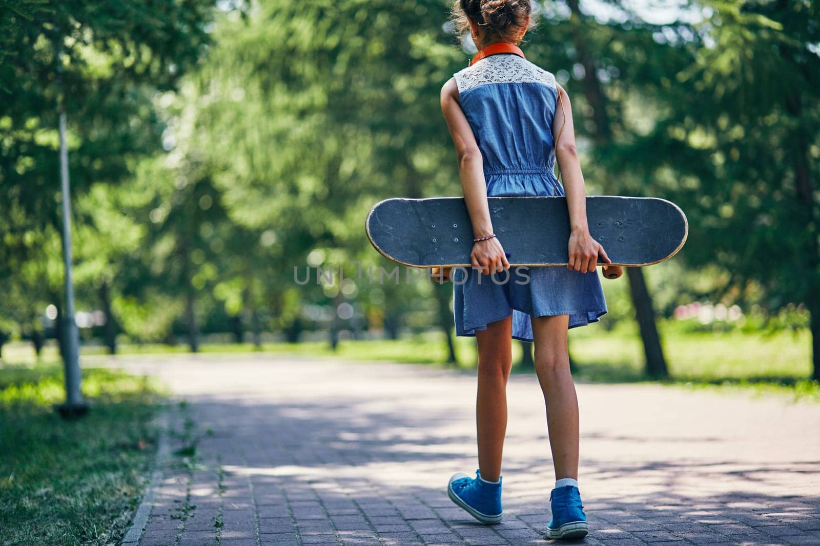 Rear view of little girl with skateboard going in park
