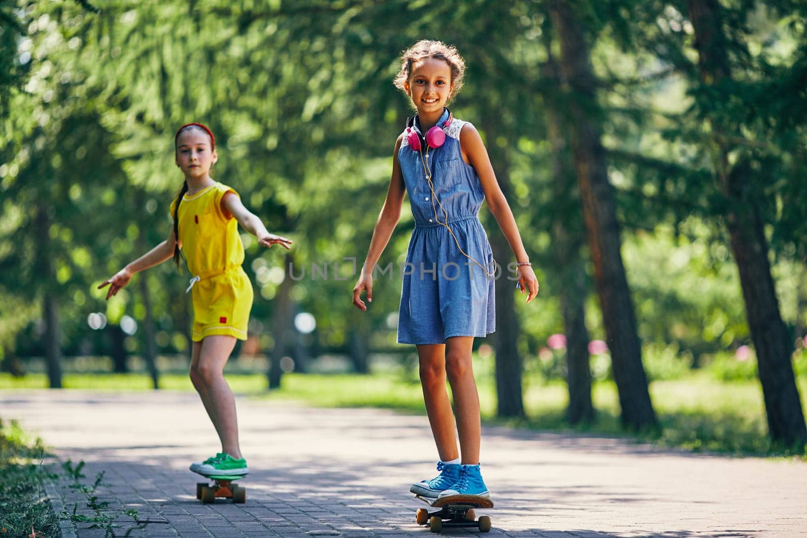 Happy cute girl and her friend skateboarding in park on summer vacations