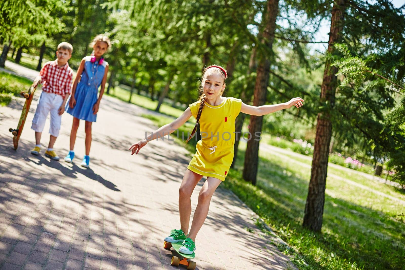 Happy girl skateboarding in park with her friends on background