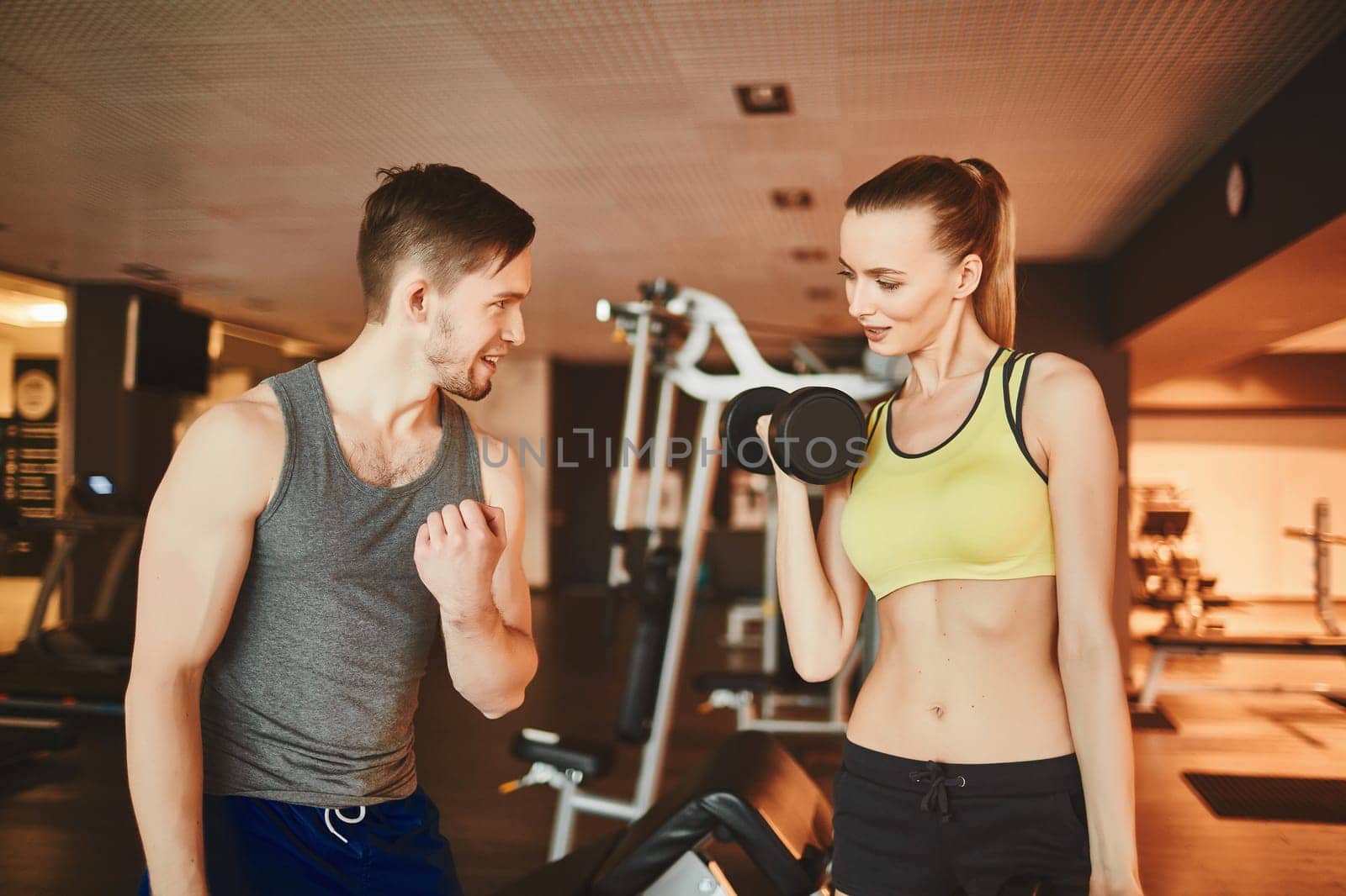 Confident trainer consulting girl with barbell in sports club