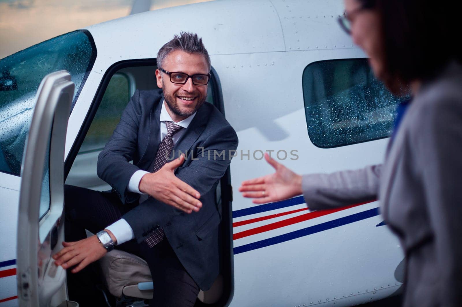 Successful businessman giving hand to his colleague while sitting in airplane