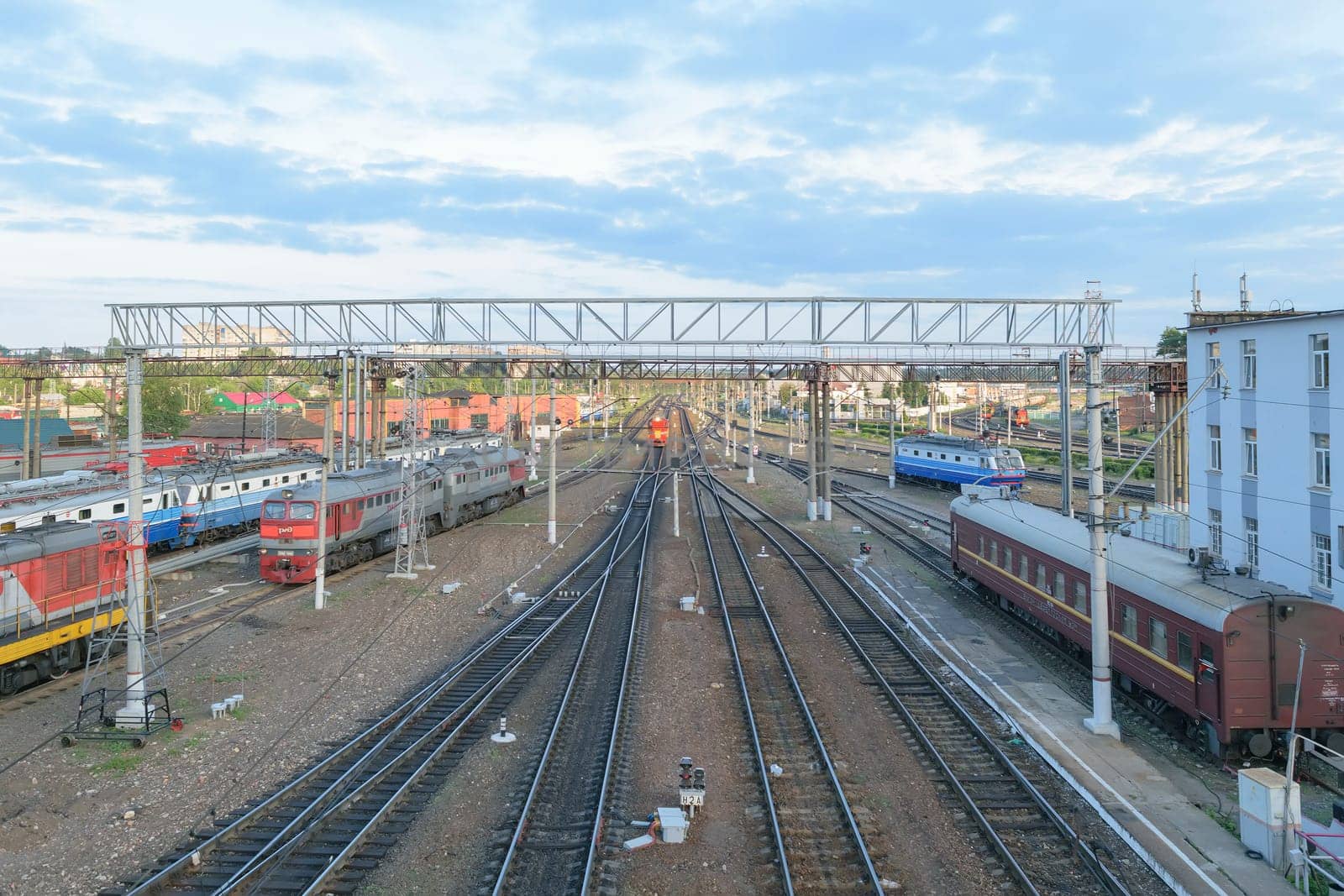 Major train station. Rails stretching into the distance. Flaw detector car is on the tracks near the building. Blue sky with a few clouds