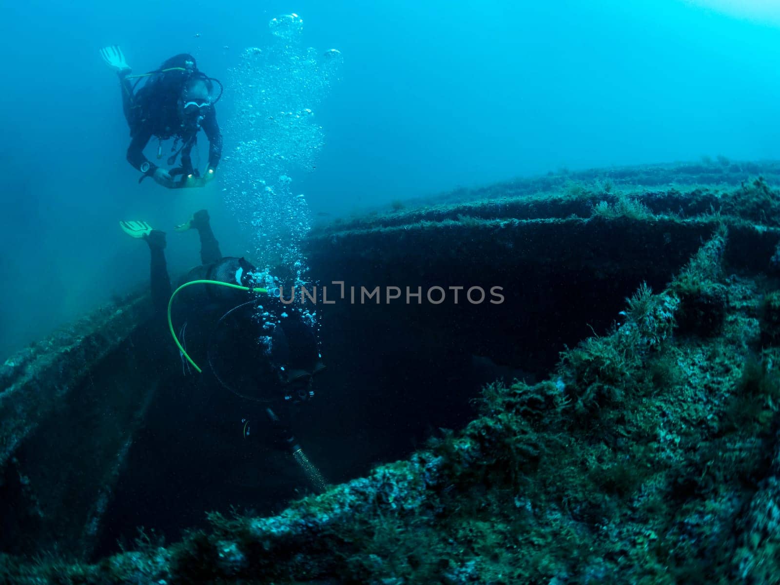 two scuba divers diving into a shipwreck, the water is dark and murky, and the man is surrounded by debris, the scene is eerie and mysterious, with the man exploring the depths of the sunken ship
