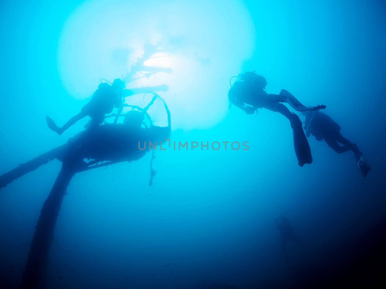 group of divers scuba diving in a wreck at ocean, the water is blue and the sun is shining brightly