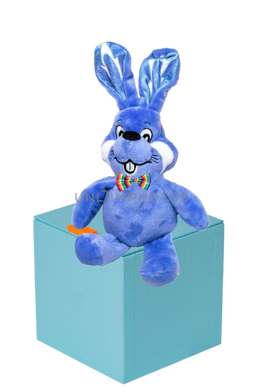 Cute blue plush bunny or rabbit with bow tie on a gift box isolated on a white background. Easter greeting card template with space for design. Bright plush toy.