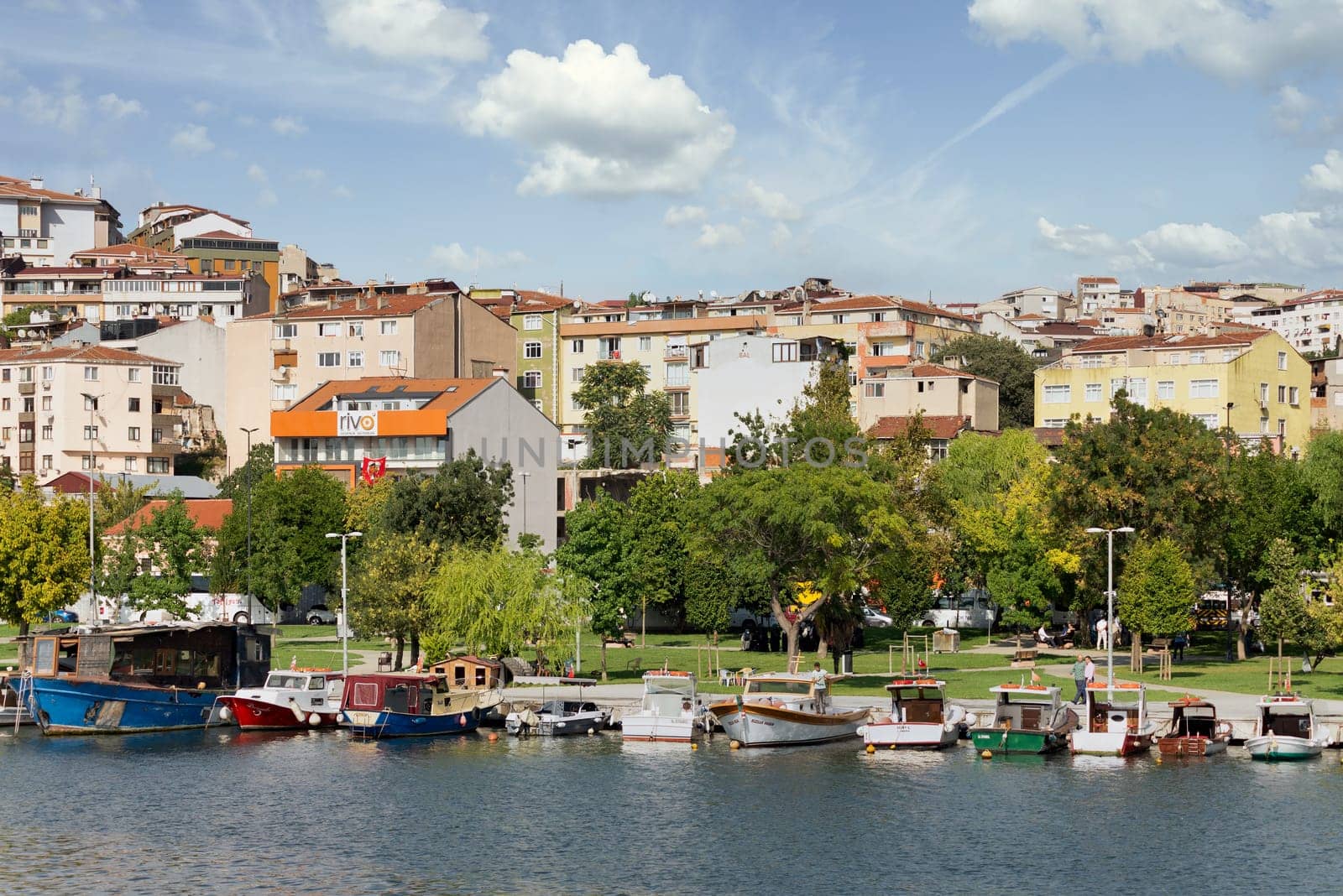 Istanbul, Turkey - September 1, 2022: Boats docked at the coast of the Golden Horn, with background of green park with dense big trees, and residential houses, in a sunny summer day