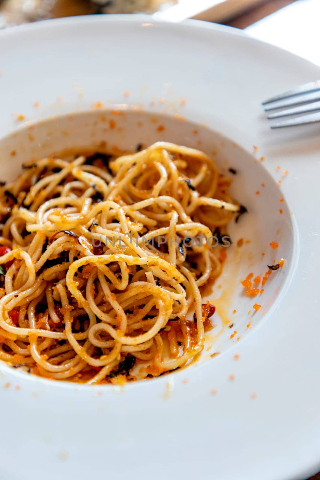 Spaghetti mixed with orange shrimp roe in a white round plate part of it has been eaten There were no vegetables on the plate at all. scattered shrimp roe convey disorder. Selective focus.