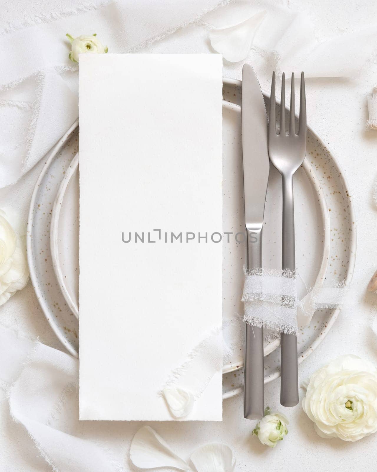 Wedding table setting with card near cream roses and white silk ribbons top view, mockup. Romantic scene with vertical menu card and pastel flowers. Valentines, Spring or Mothers day concept