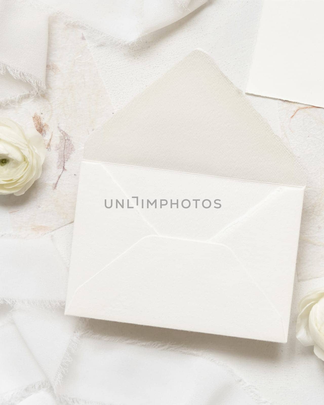 Blank envelope near cream roses and white silk ribbons top view, wedding mockup. Romantic scene with pastel flowers flat lay. Valentines, Spring or Mothers day concept