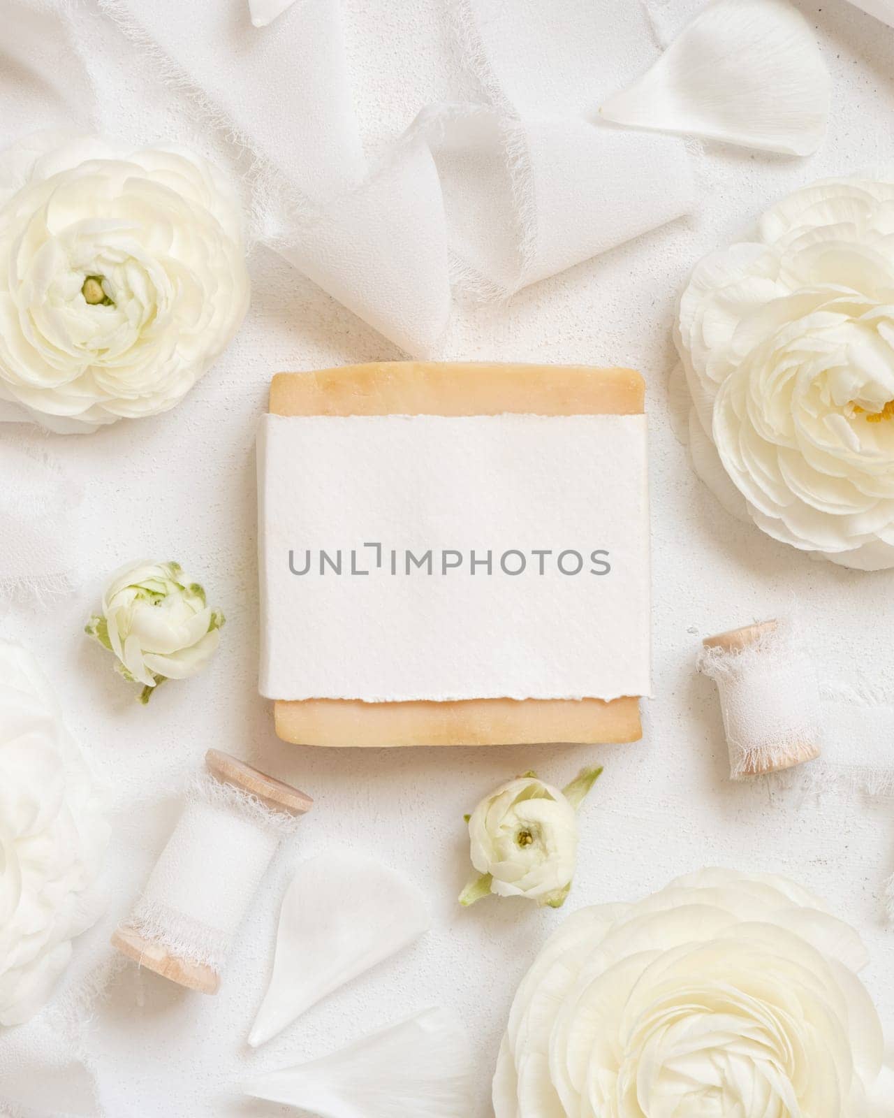 Handmade soap bar with blank label near cream roses and white ribbons top view, soap mockup. Beauty product for face and body care. Natural Spa cosmetic concept