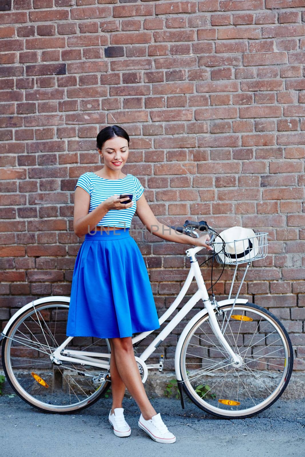 Cute girl with bicycle using cellphone against brick wall