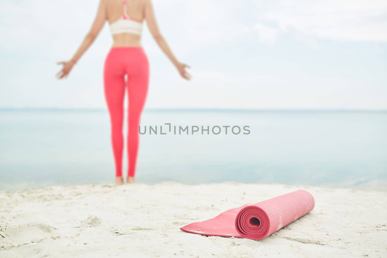 Red rolled mat for yoga on background of young woman standing by water