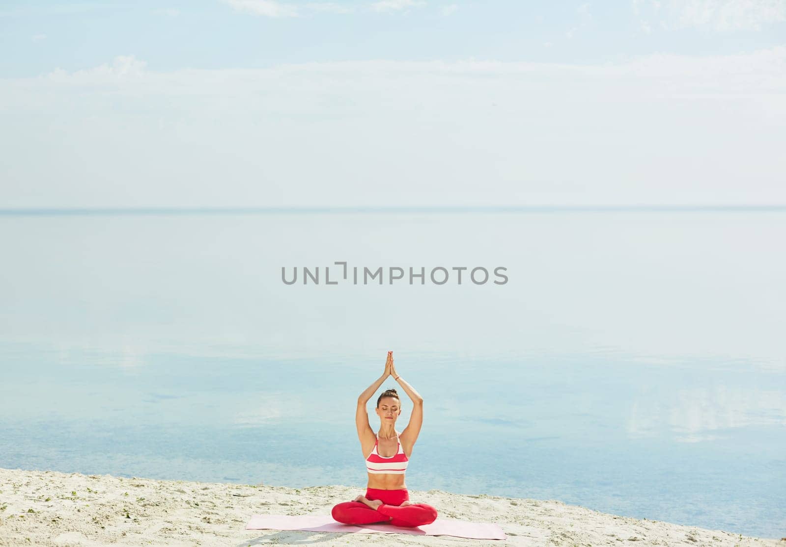 Young woman practicing yoga on sand by water