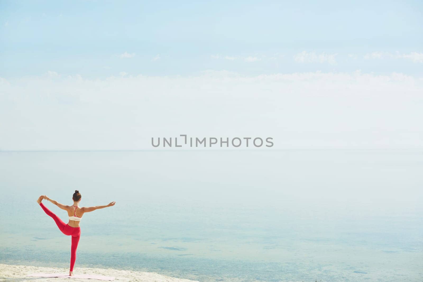 Back view of fit female stretching her leg while standing on the beach