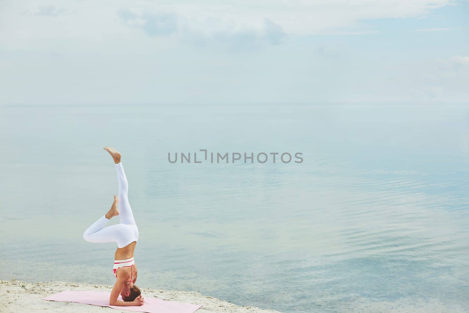 Attractive woman keeping balance while standing on her head on sandy beach