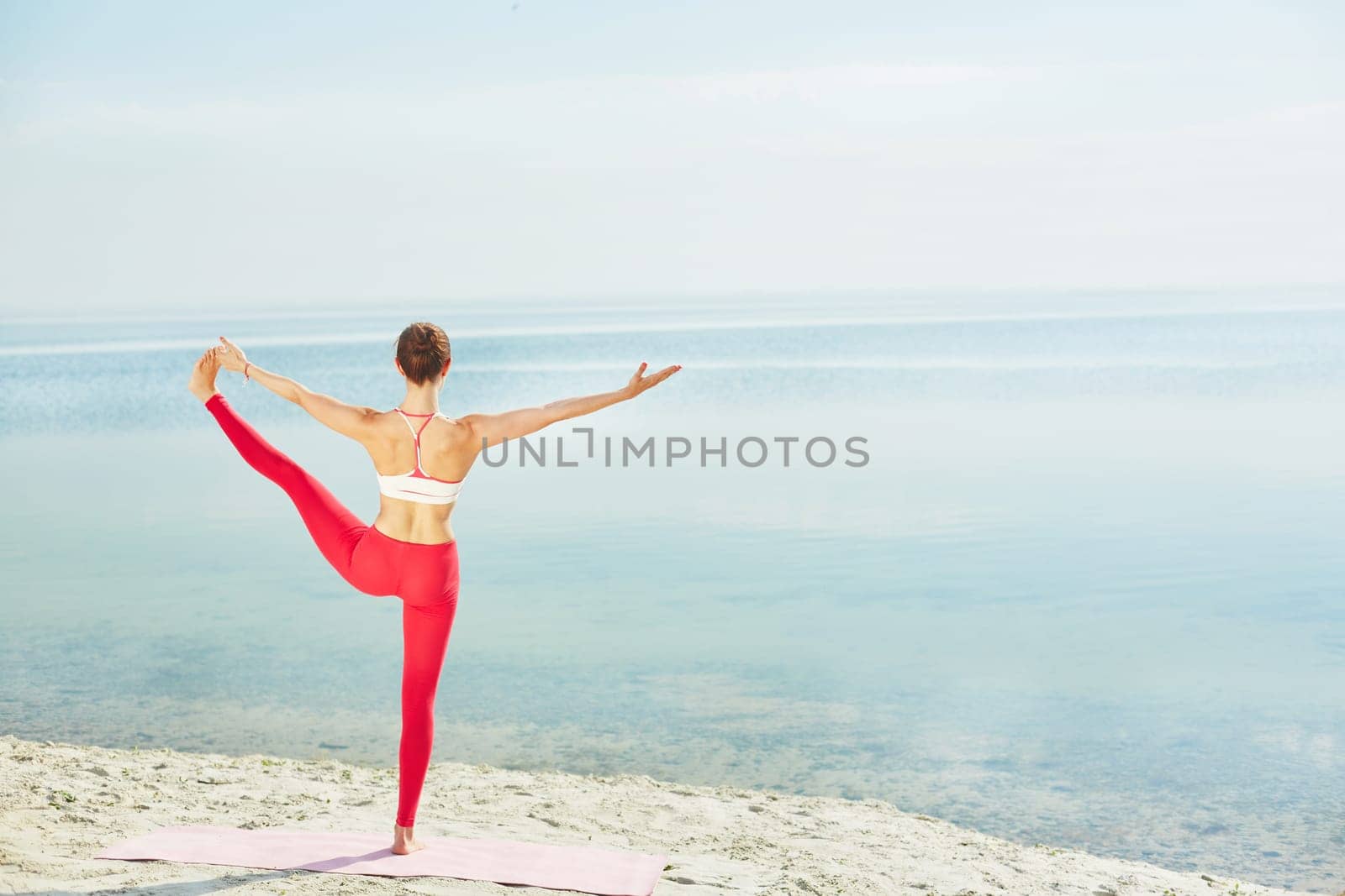 Sporty female in activewear stretching her leg while standing on the beach