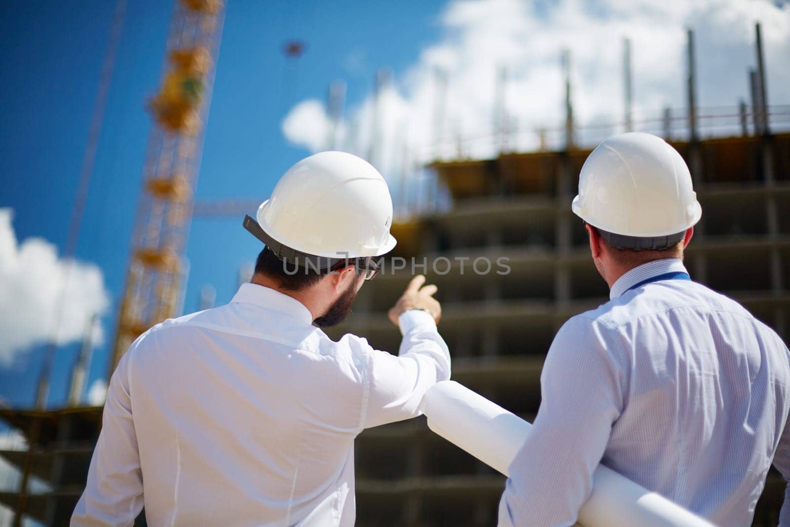 Rear view of architects looking at construction while one of them showing it to colleague