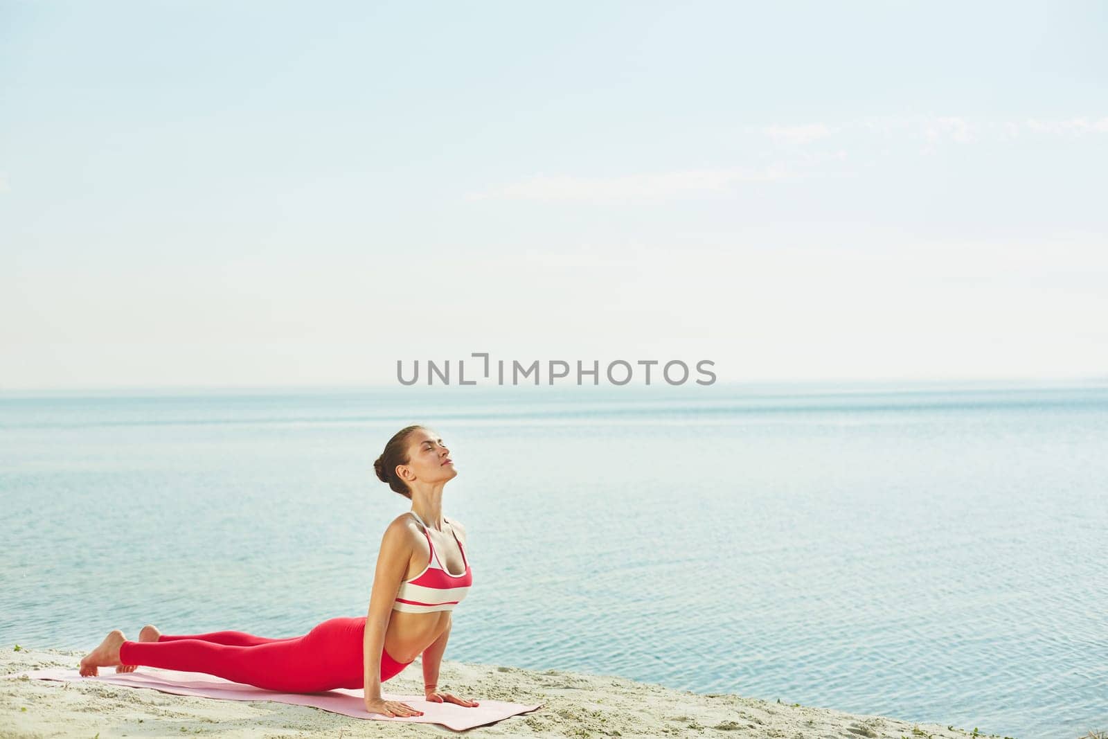 Fit woman doing stretching exercise on mat by water