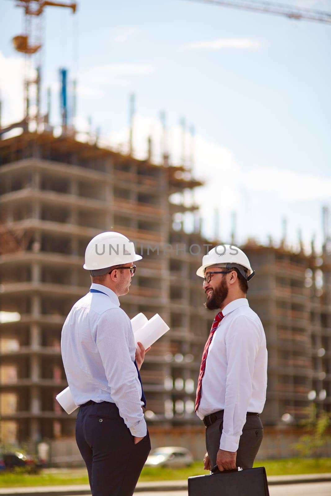 Modern businessmen in helmets interacting in front of unfinished construction