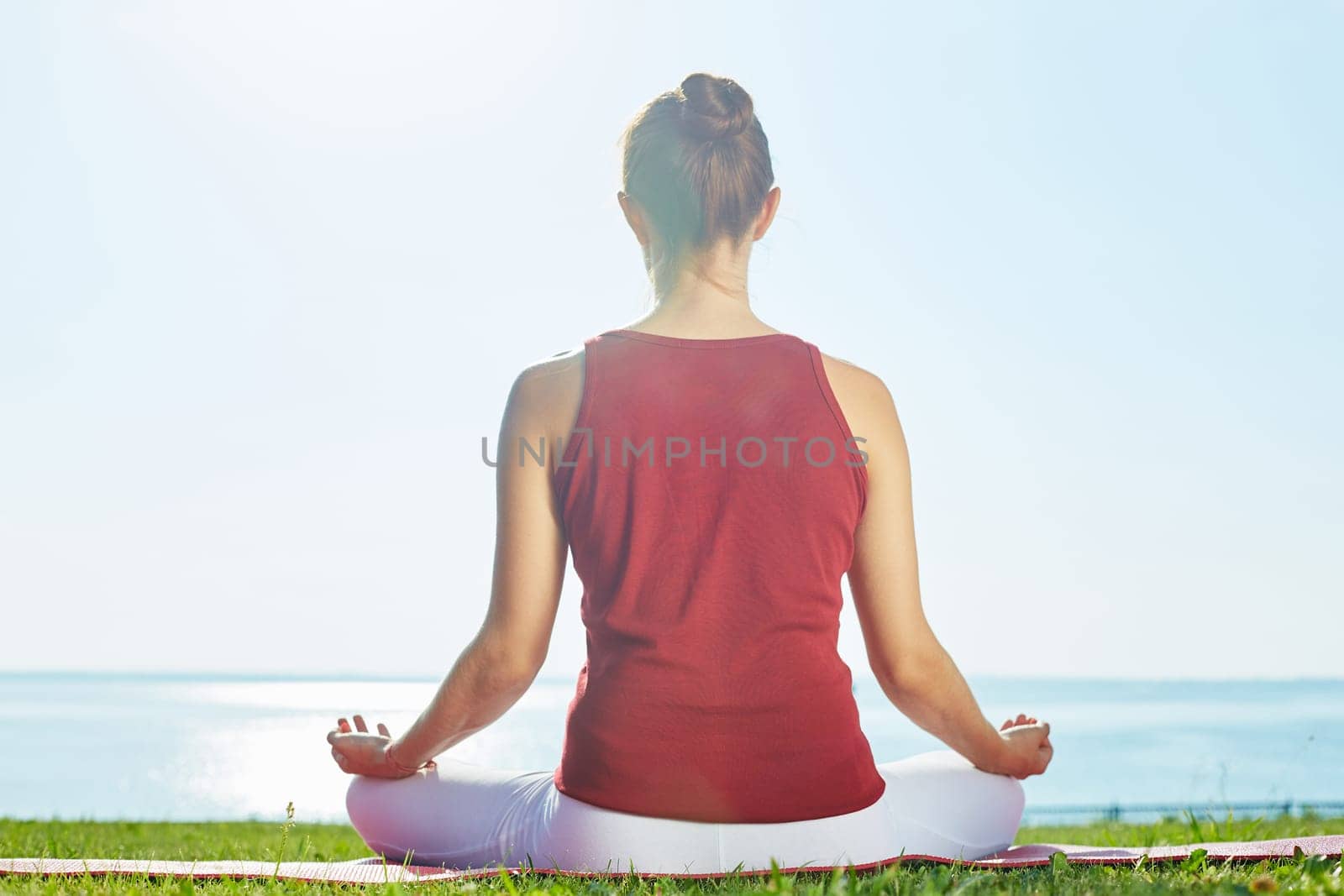 Back of young woman meditating by the seaside