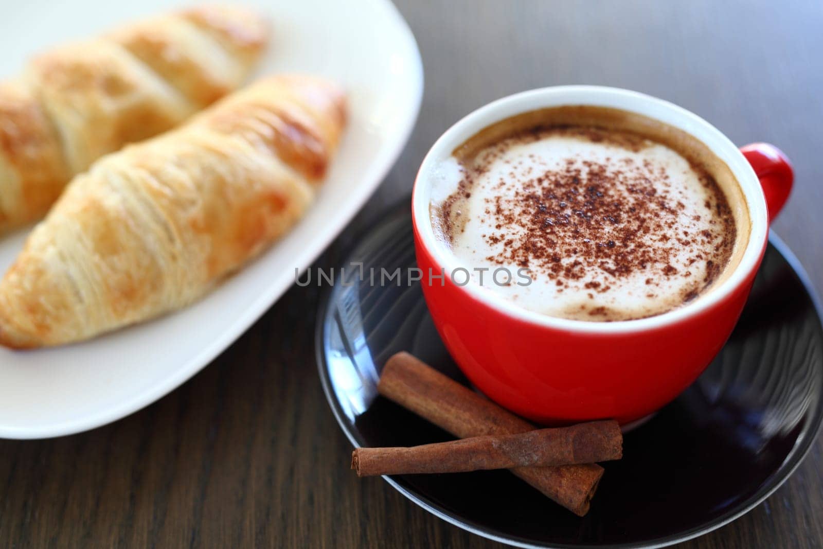 An italian cappuccino served with cocoa and croissant with intentional blurred background