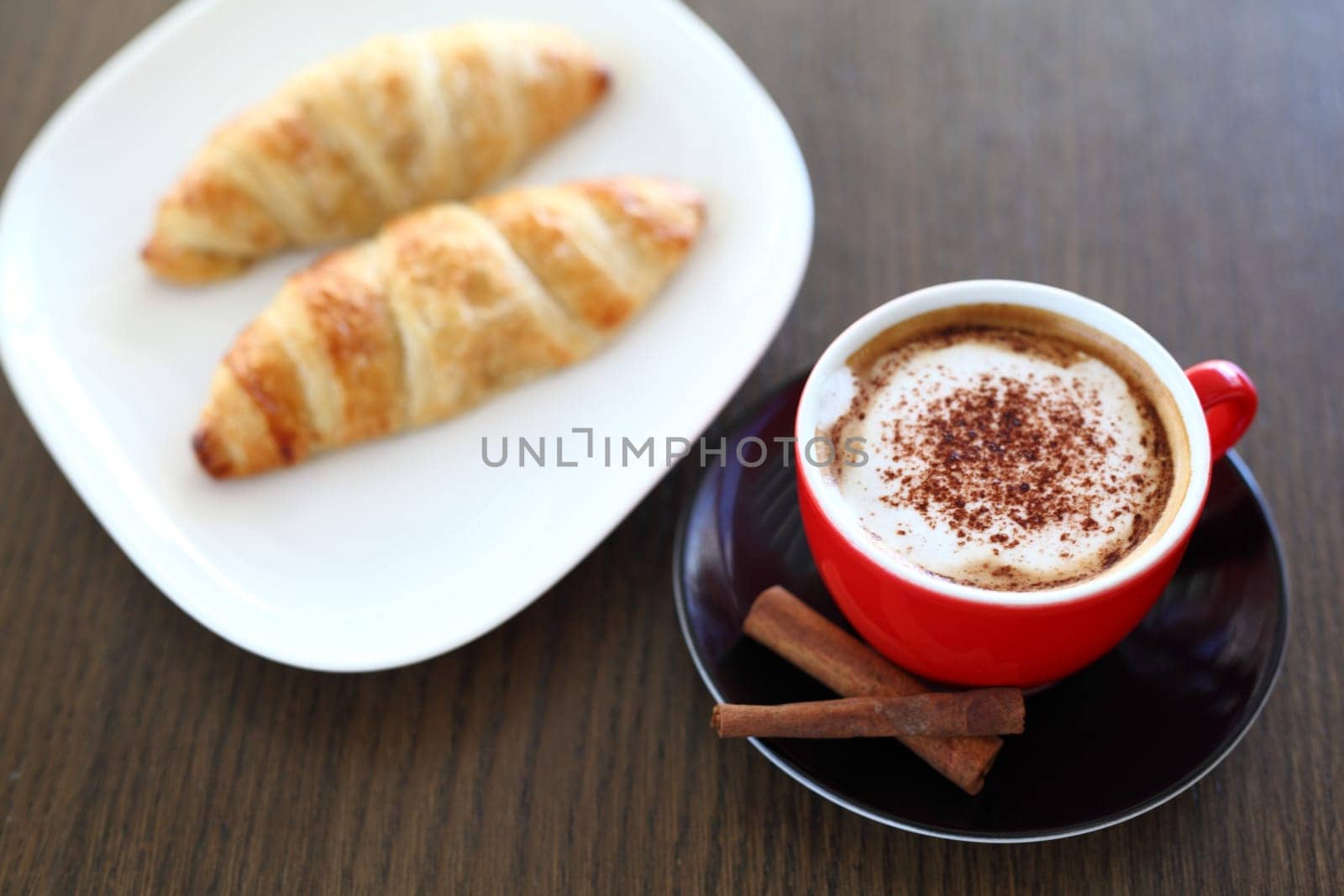 An italian cappuccino served with cocoa and croissant with intentional blurred background