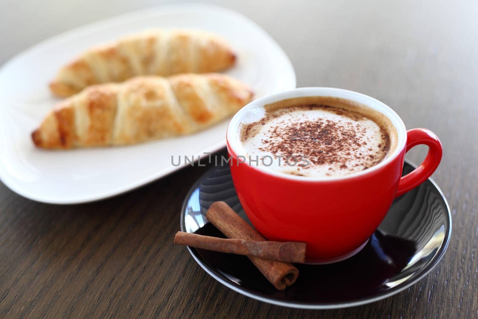 An italian cappuccino served with cocoa and croissant with intentional blurred background