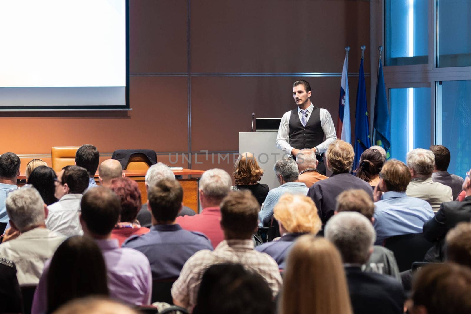 Speaker giving a talk in conference hall at business meeting event. Rear view of unrecognizable people in audience at the conference hall. Business and entrepreneurship concept.