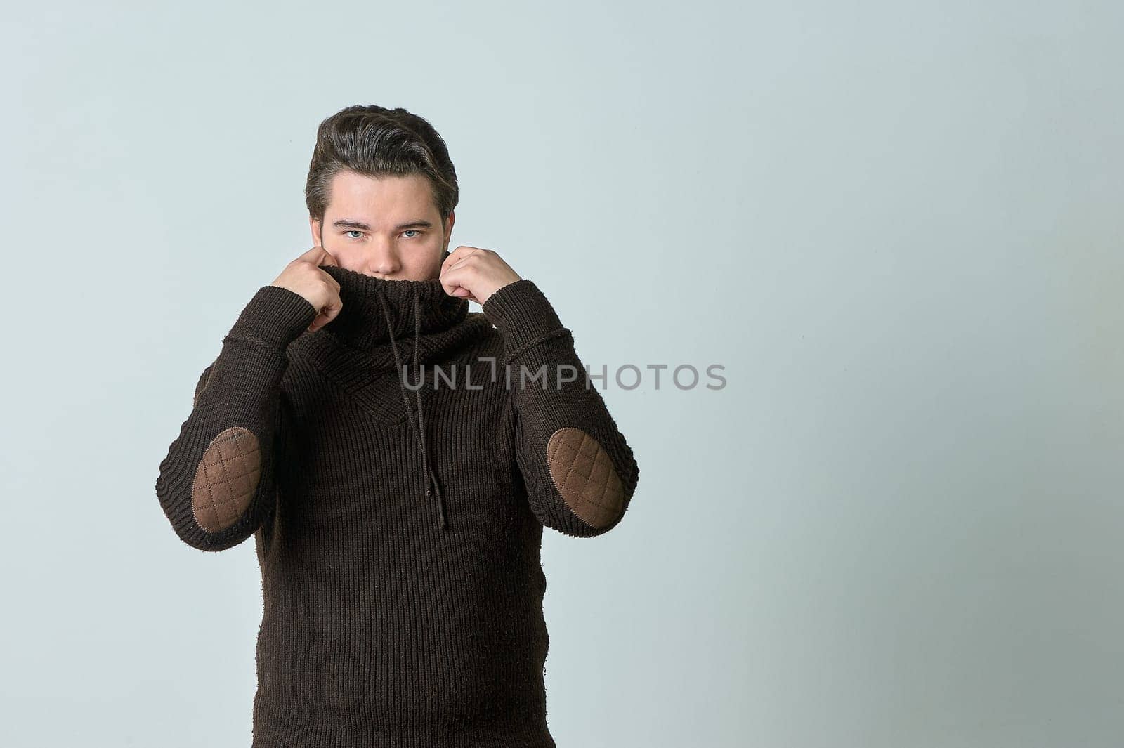 a man wraps himself in a brown sweater against the cold on a gray background. High quality photo