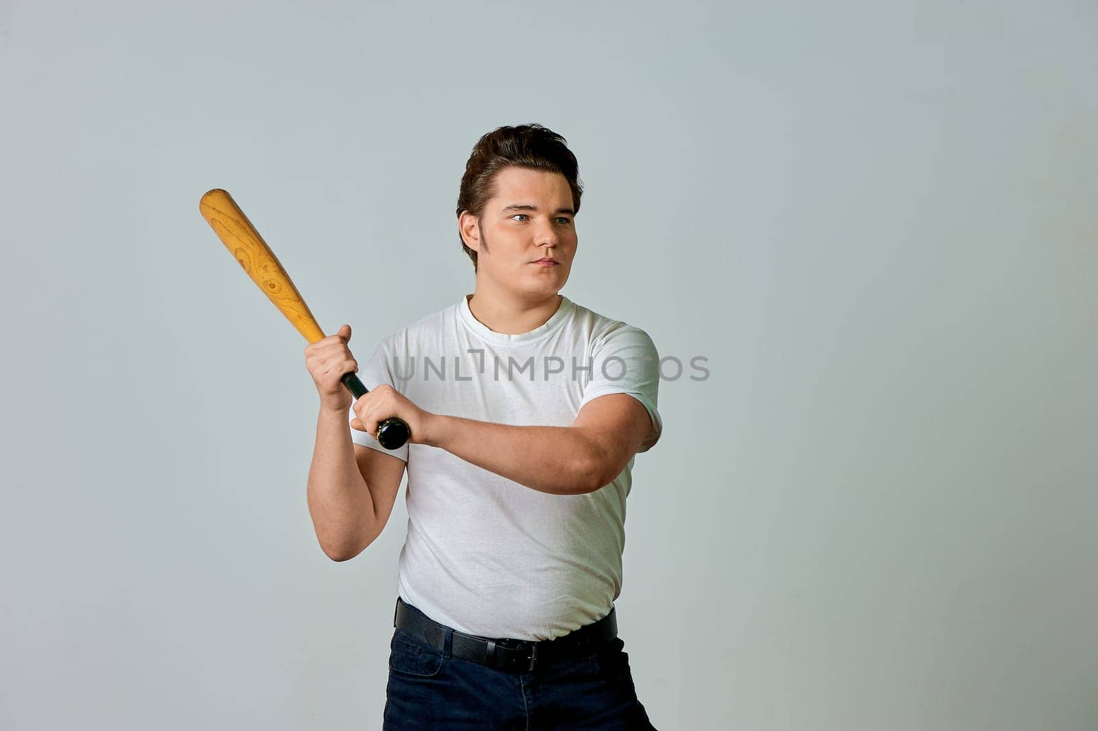 A man with a bat in his hands swings on a gray background. High quality photo