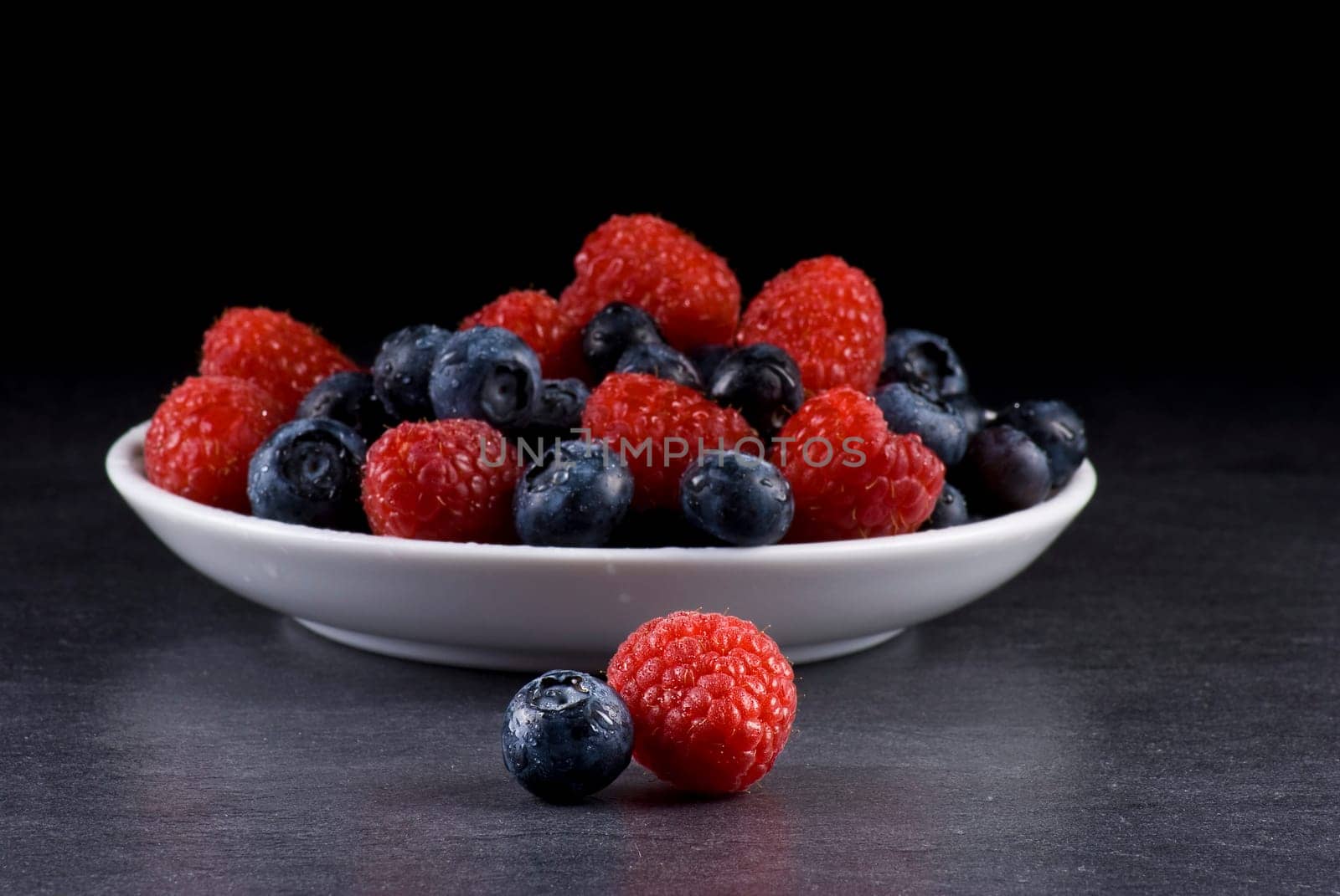 Plate of fresh blueberries and raspberries on balck background