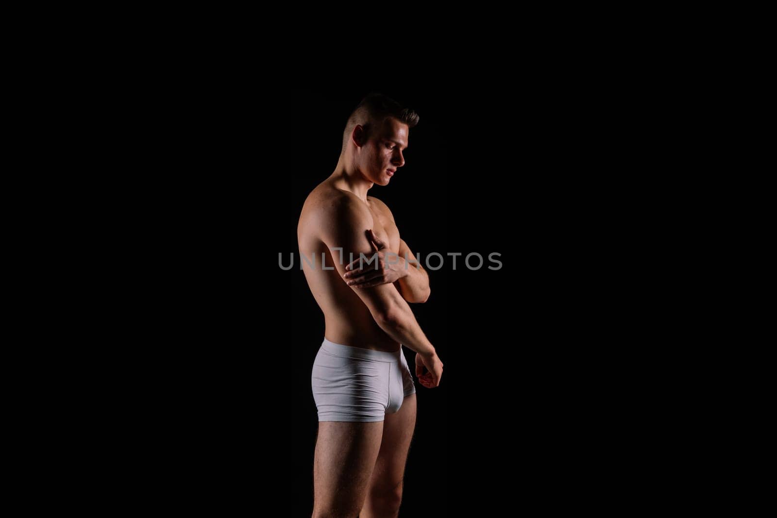 Shirtless bodybuilder holding a dumbell and showing his muscular arms.