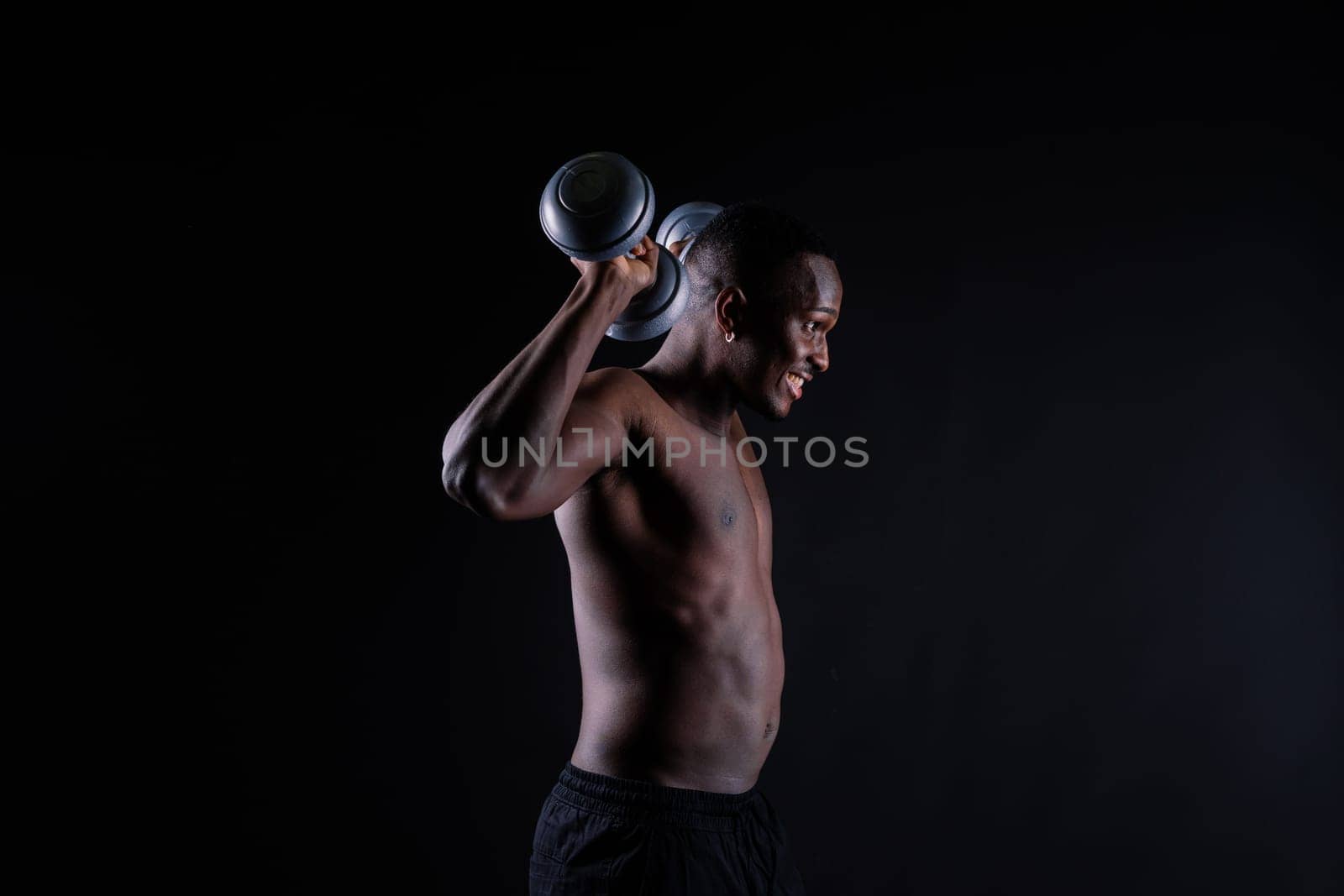 Isolated african muscular man with dumbbells on a dark studio background. Strong shirtless black guy