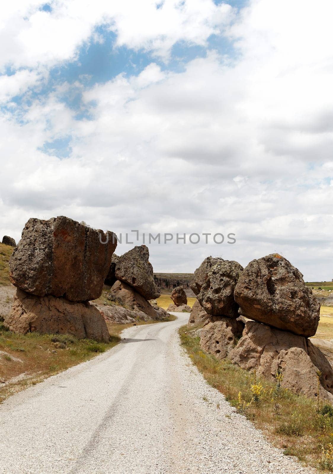 precarious balanced volcanic rocks on either side of a public dirt track, Cappadocia, Turkey. Volcanic terrian, lava rock, limestone, sandstone, blue cloud layered sky, portrait, copy space, crop area, scenic