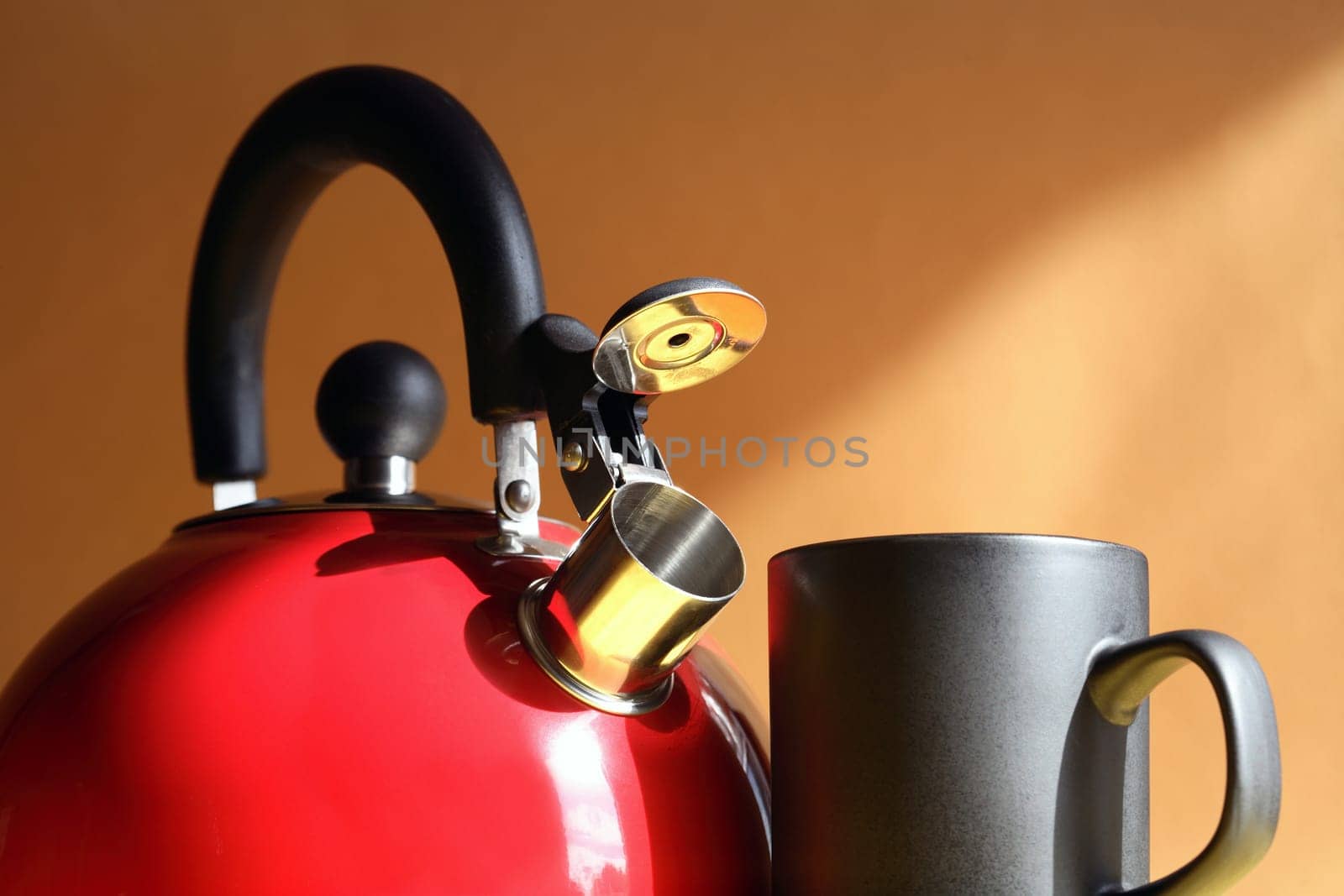 Closeup of red metal kettle near black mug on background with sunbeam