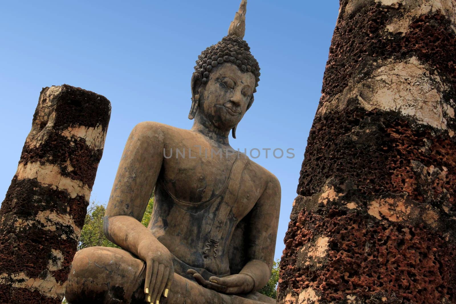 large seated buddha with gold leaf on fingernails in sukhothai historical park temple ruins in northern thailand