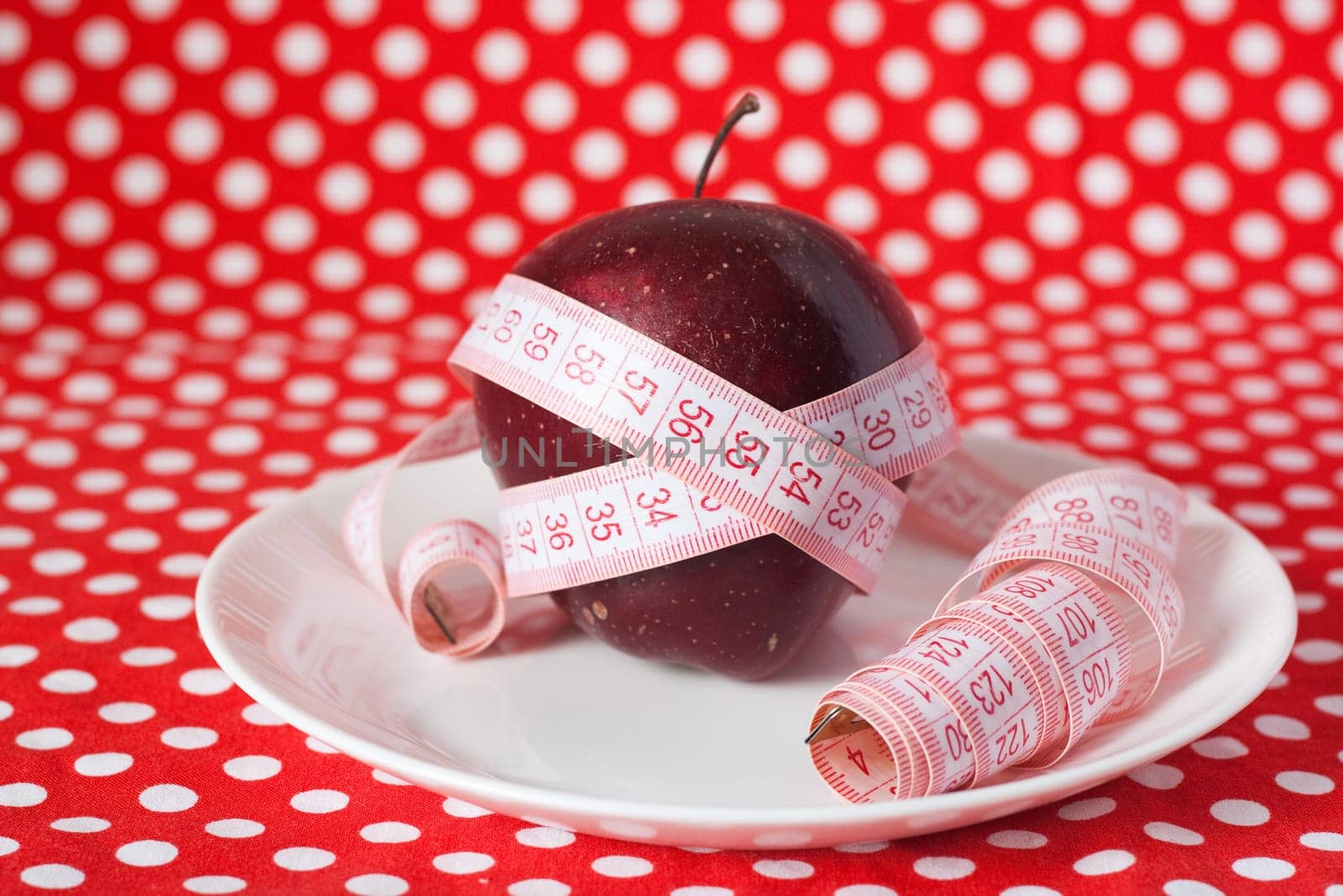 Red apple and measuring tape on a white plate