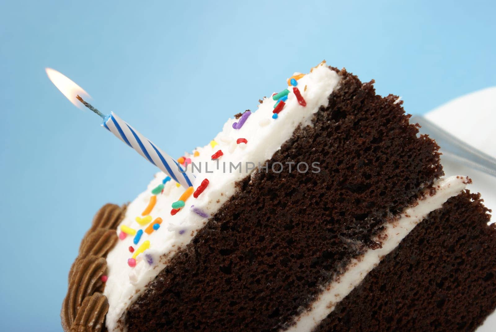 A slice of chocolate cake with a single lit candle.