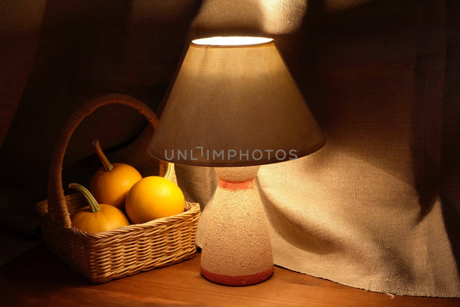 Basket with three pumpkins near luminous desk lamp on canvas background