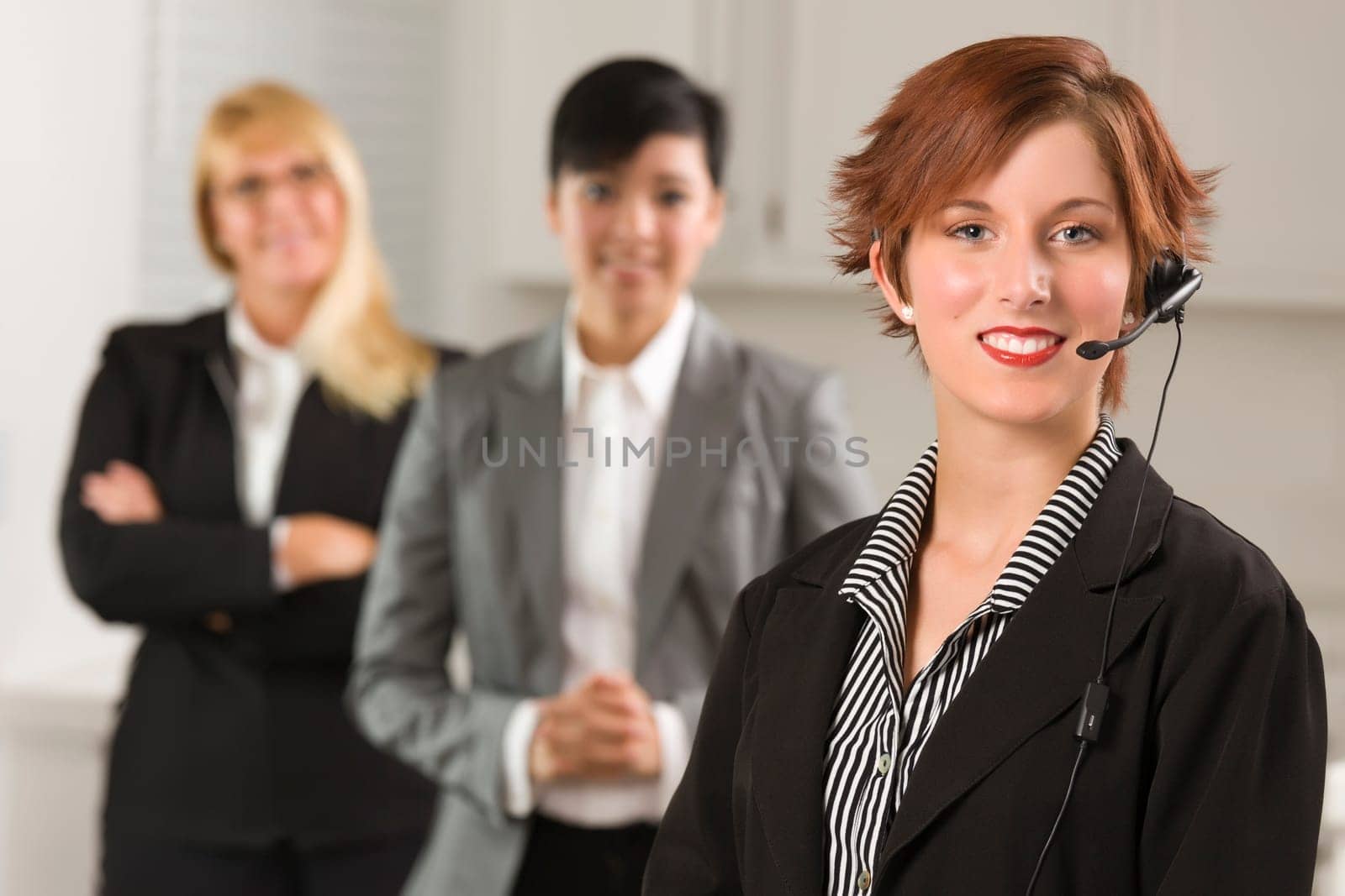 Pretty Red Haired Businesswoman with Headset and Colleagues Behind in Office Setting.