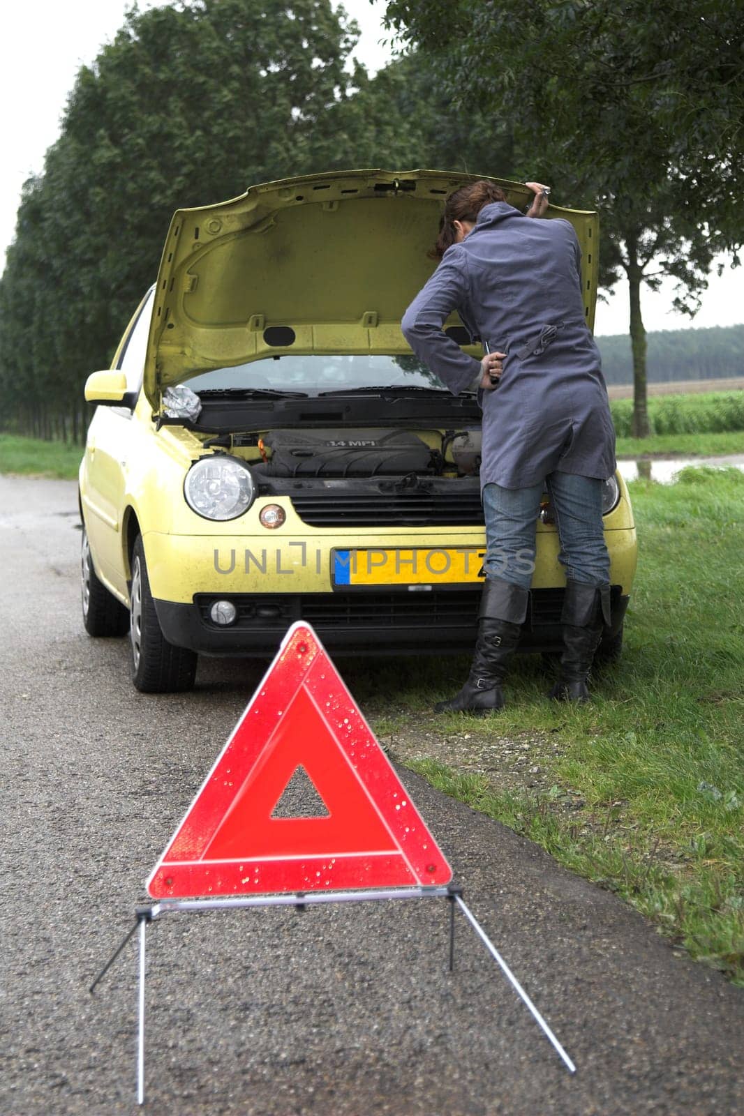 Pretty brunette bend over the insides of her car (focus on the girl) with danger triangle in front