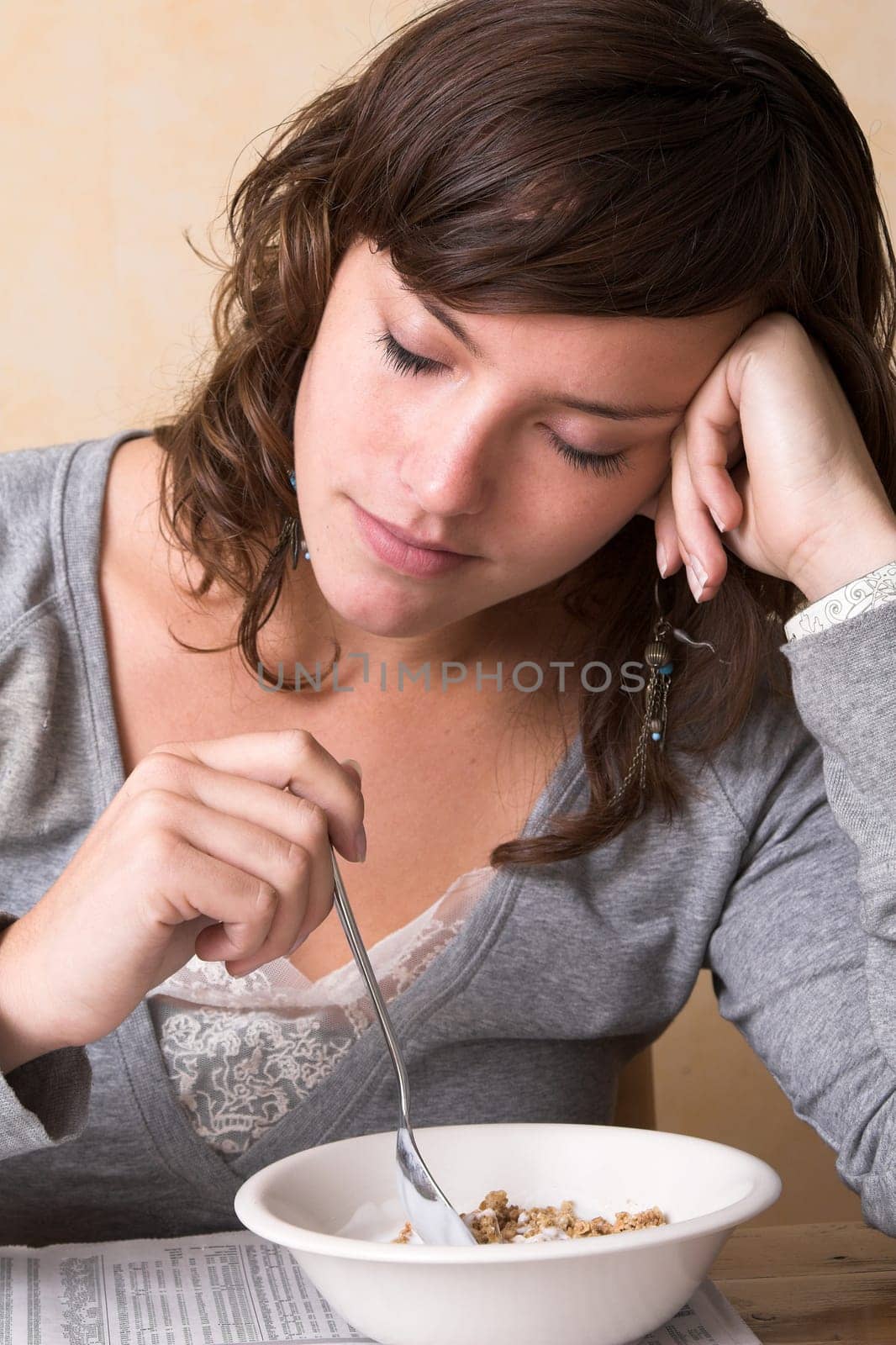 Pretty brunette closing her eyes, still feeling sleepy while having breakfast
